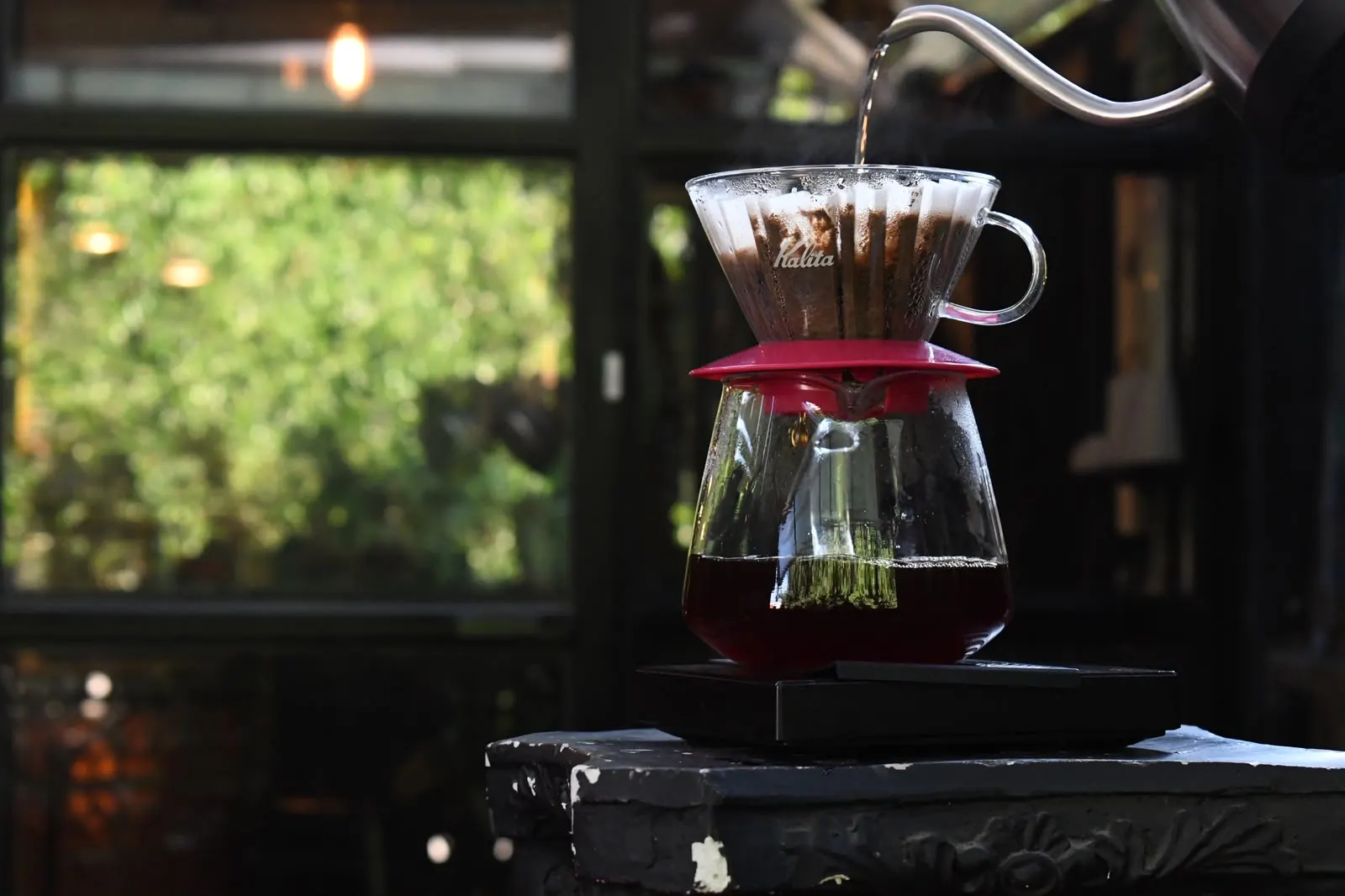 Dripper Kalita de cristal sobre su jarra, con agua cayendo de una tetera de cuello de ganso