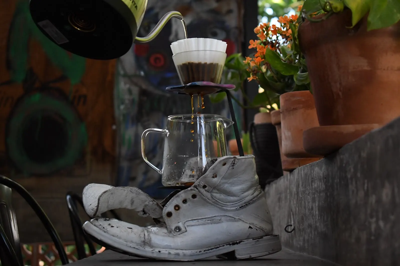 Dripper Orea con filtro ondulado goteando café en una jarra de cristal, entre macetas