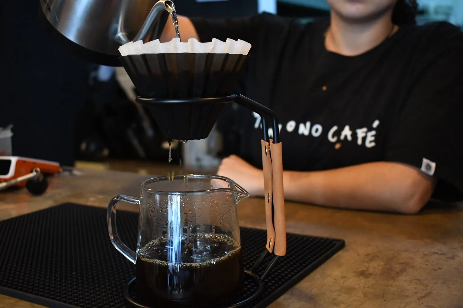 Dripper Origami negro de pliegues verticales montado en su soporte, goteando café en Monono Coffee